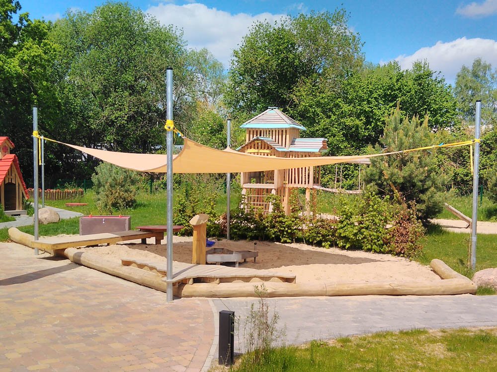 Sandspielbereich mit Sonnensegel, Holzspielhaus und Kletterelementen im Au&szlig;enbereich